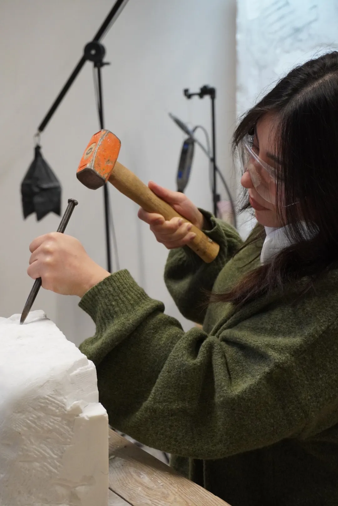 Frida talla un bloque de mármol con maceta y cincel, con gafas de protección